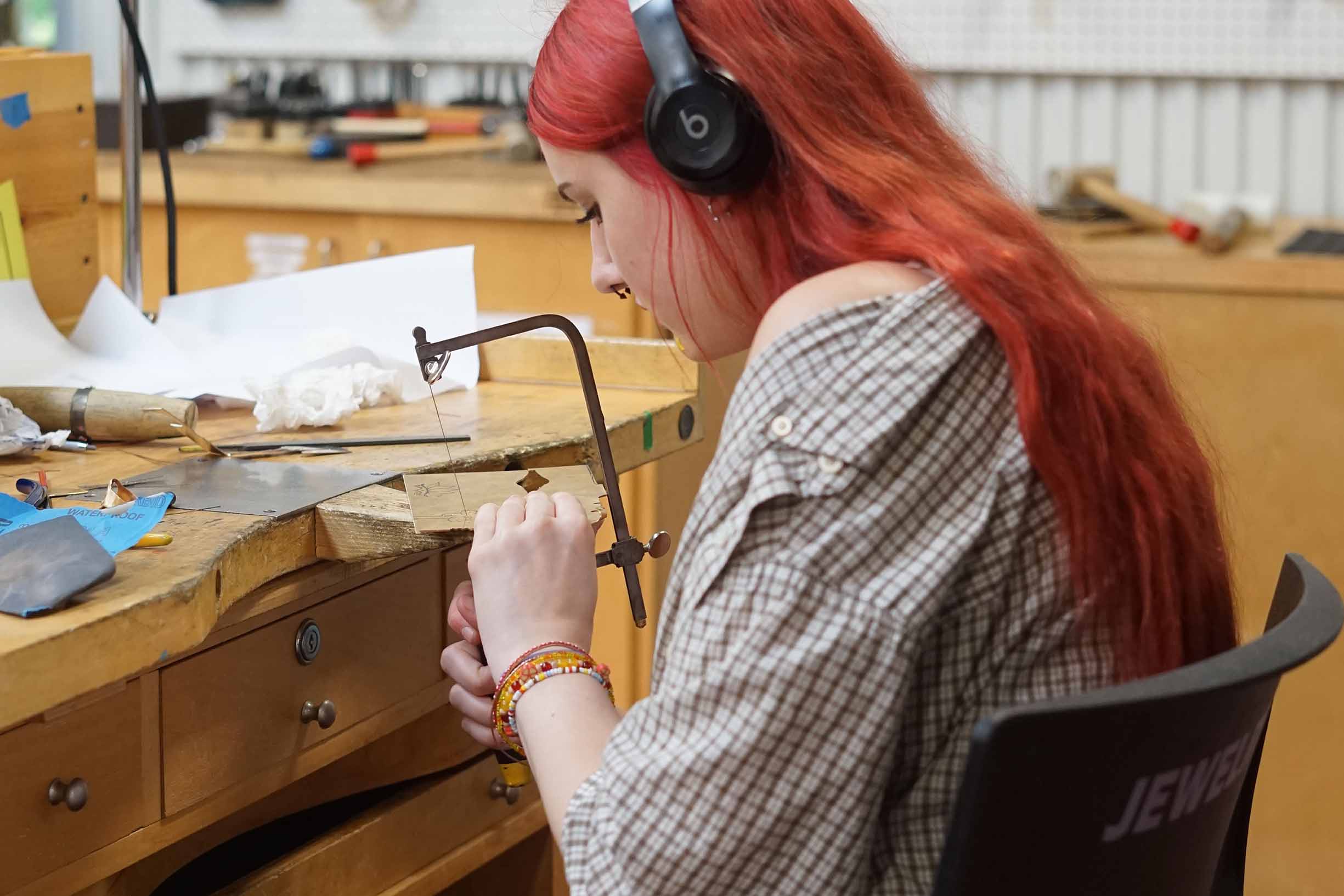Student creating jewelry with a saw at a workbench
