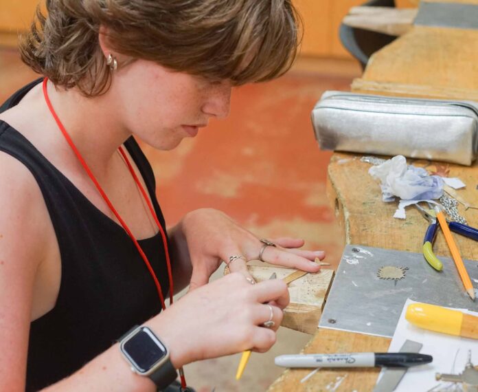 Student creating jewelry with device at a workbench