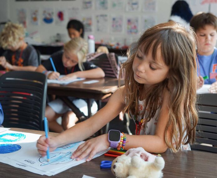 Female student coloring some planets on a piece of paper in a classroom.