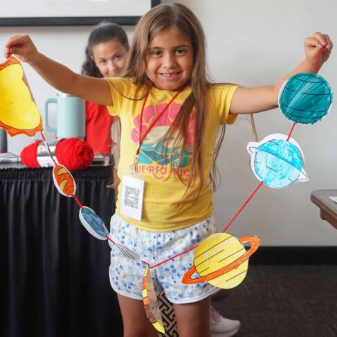 student holding her string of paper planets in the solar system in a classroom
