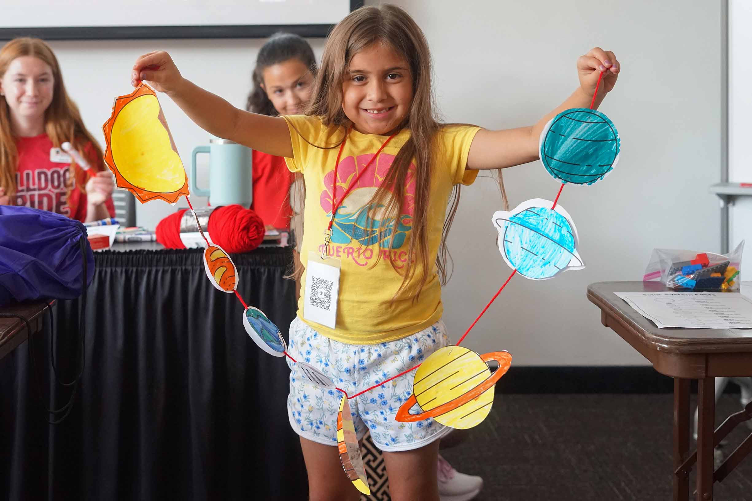 student holding her string of paper planets in the solar system in a classroom