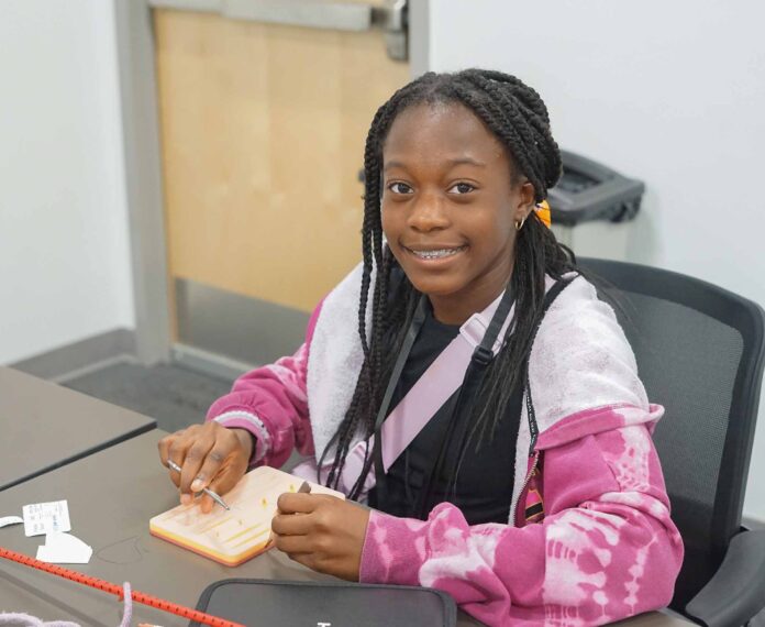female student using a stitching kit sitting in a classroom