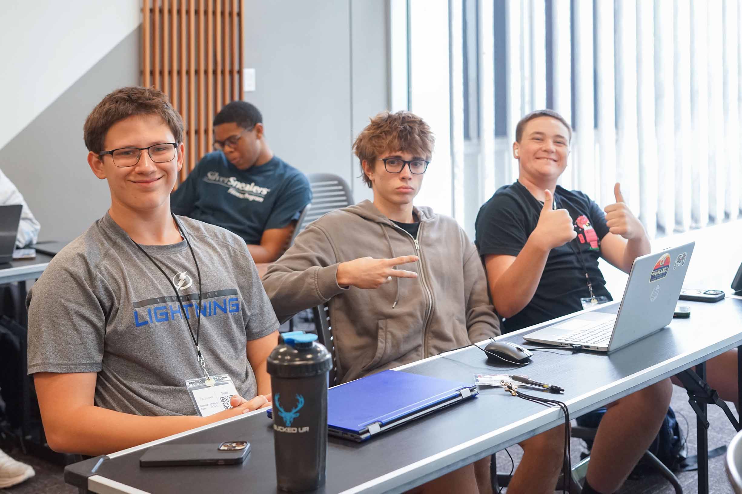 three male student sitting in a classroom in front of a couple of laptops waiting for the mock trial camp to start