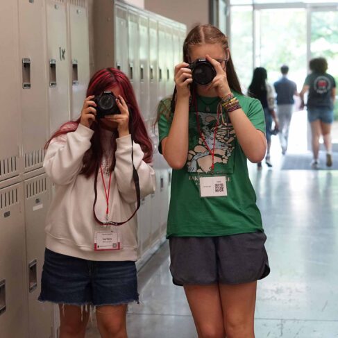 two female students standing in a hallway looking through Cannon cameras