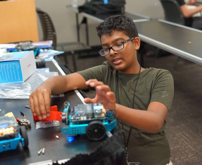 student assembling his robot sitting at a desk in a classroom