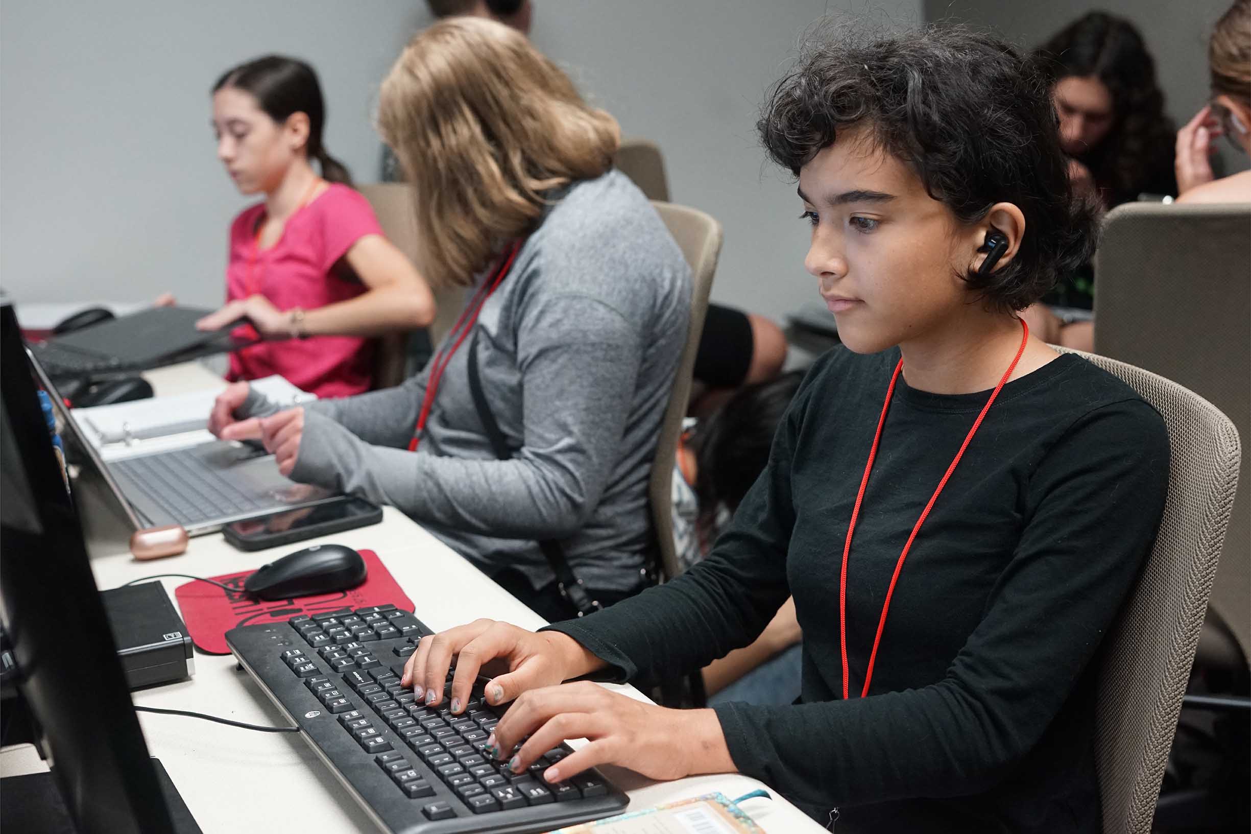A student typing on a computer in a classroom full of students.