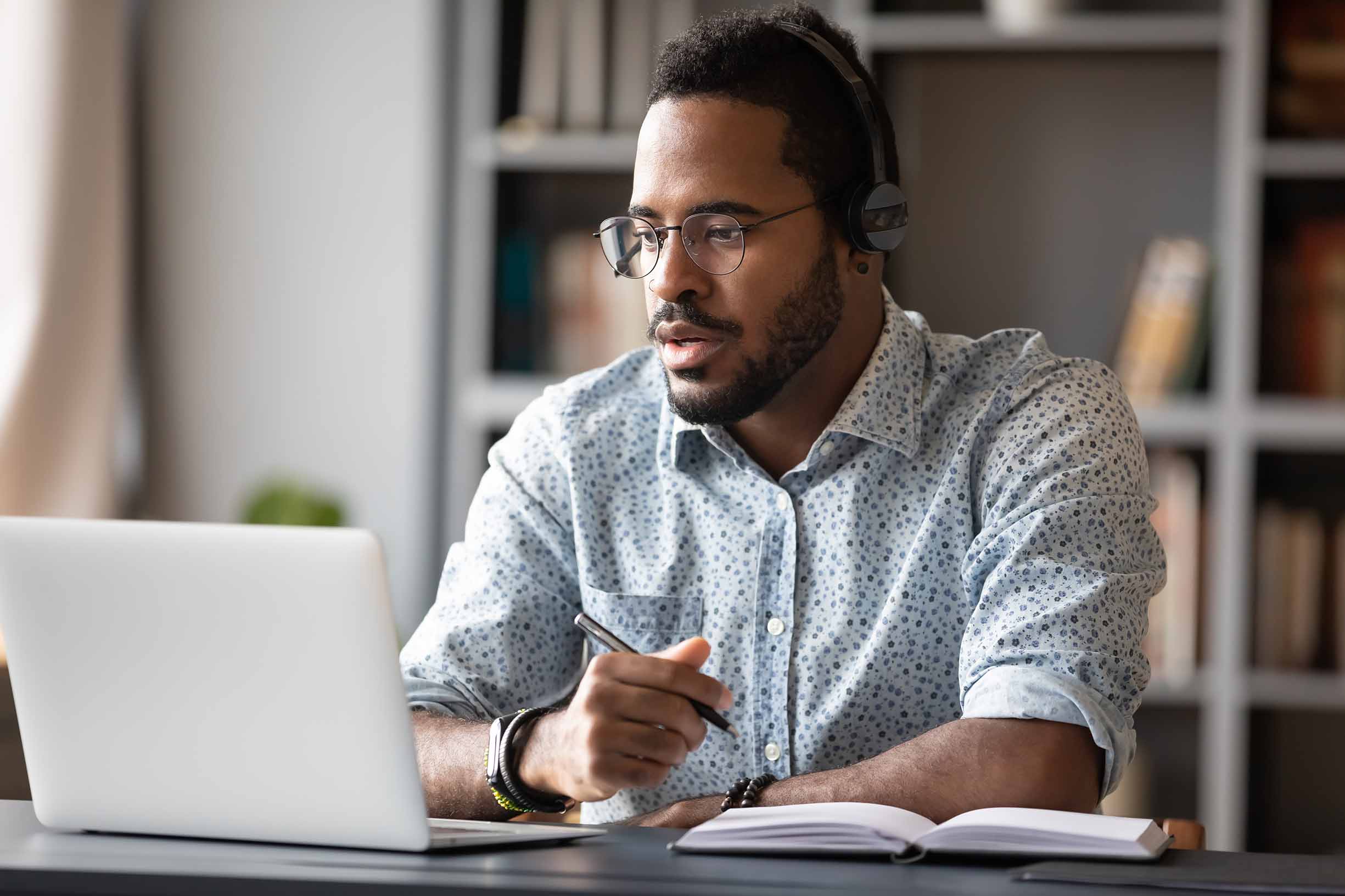 Focused student wearing headphones study online learning education course conference calling make notes sit at work desk.