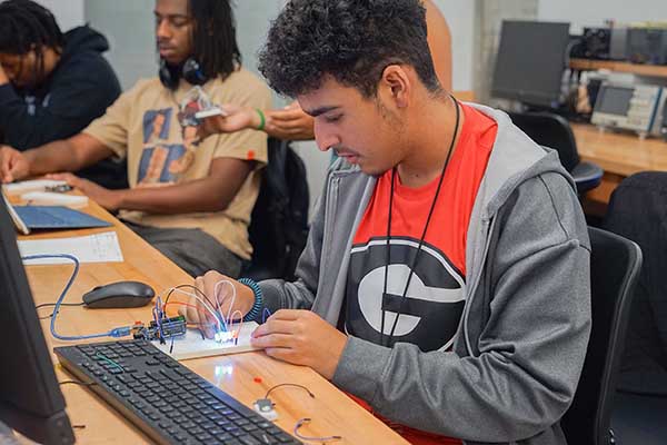 A student sitting in front of a computer working on electrical board in a classroom