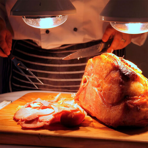 a chef carving a roasted ham on a wood board