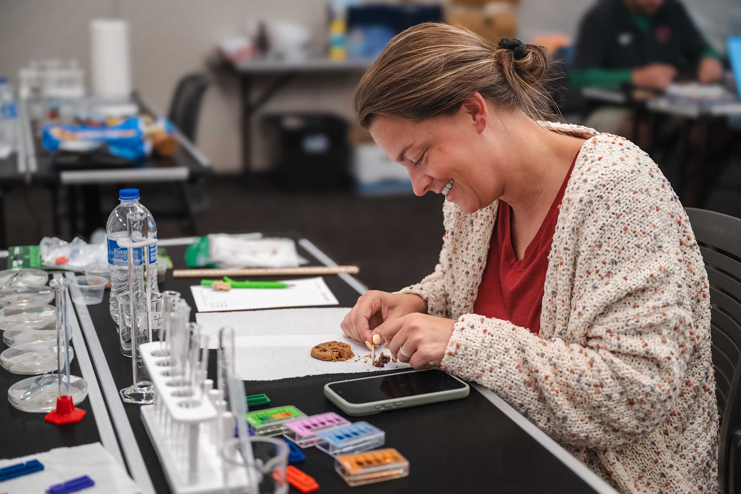 Woman analyzing food sitting in front of test tubes and recording data.